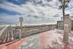 Un muelle de madera que conduce a la playa, con un cartel y pilares.