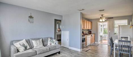 Una sala de estar moderna con un sofá gris, una alfombra mullida y una cocina al fondo.