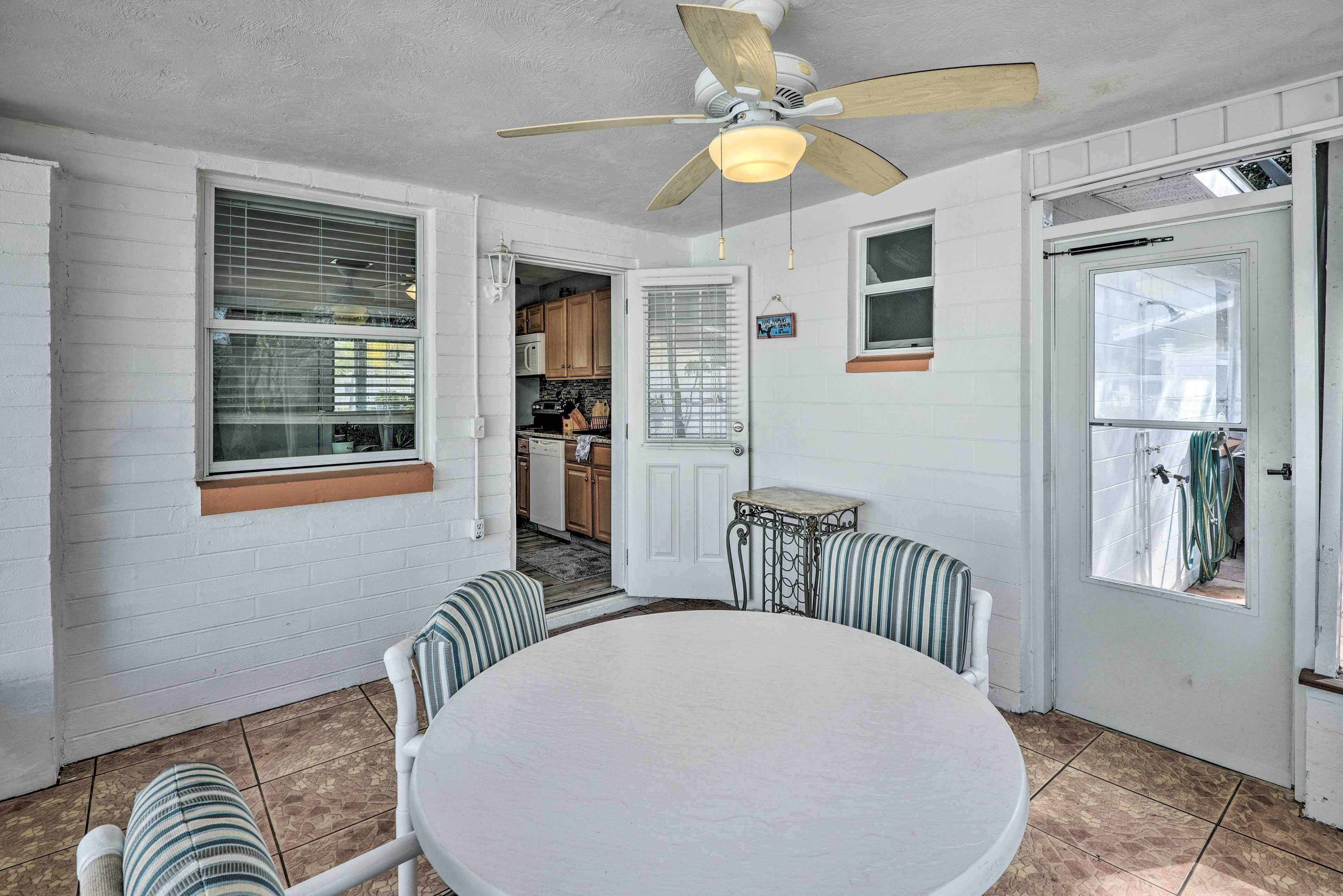 Une cuisine aux murs en briques blanches, une table à manger avec des chaises à rayures, un ventilateur de plafond et une vue sur la cuisine adjacente.