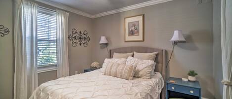 A bedroom with a bed, two bedside tables, a ceiling fan, a window with curtains, and wall decor.