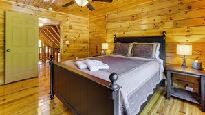 A wooden-paneled room with a bed, a ceiling fan, and a nightstand with a lamp. - Lake Hartwell Cabin, Perfect for Clemson Game Day (Fair Play)