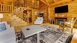 A log cabin interior with a staircase, a fireplace, a television, and a cozy seating area. - Lake Hartwell Cabin, Perfect for Clemson Game Day (Fair Play)