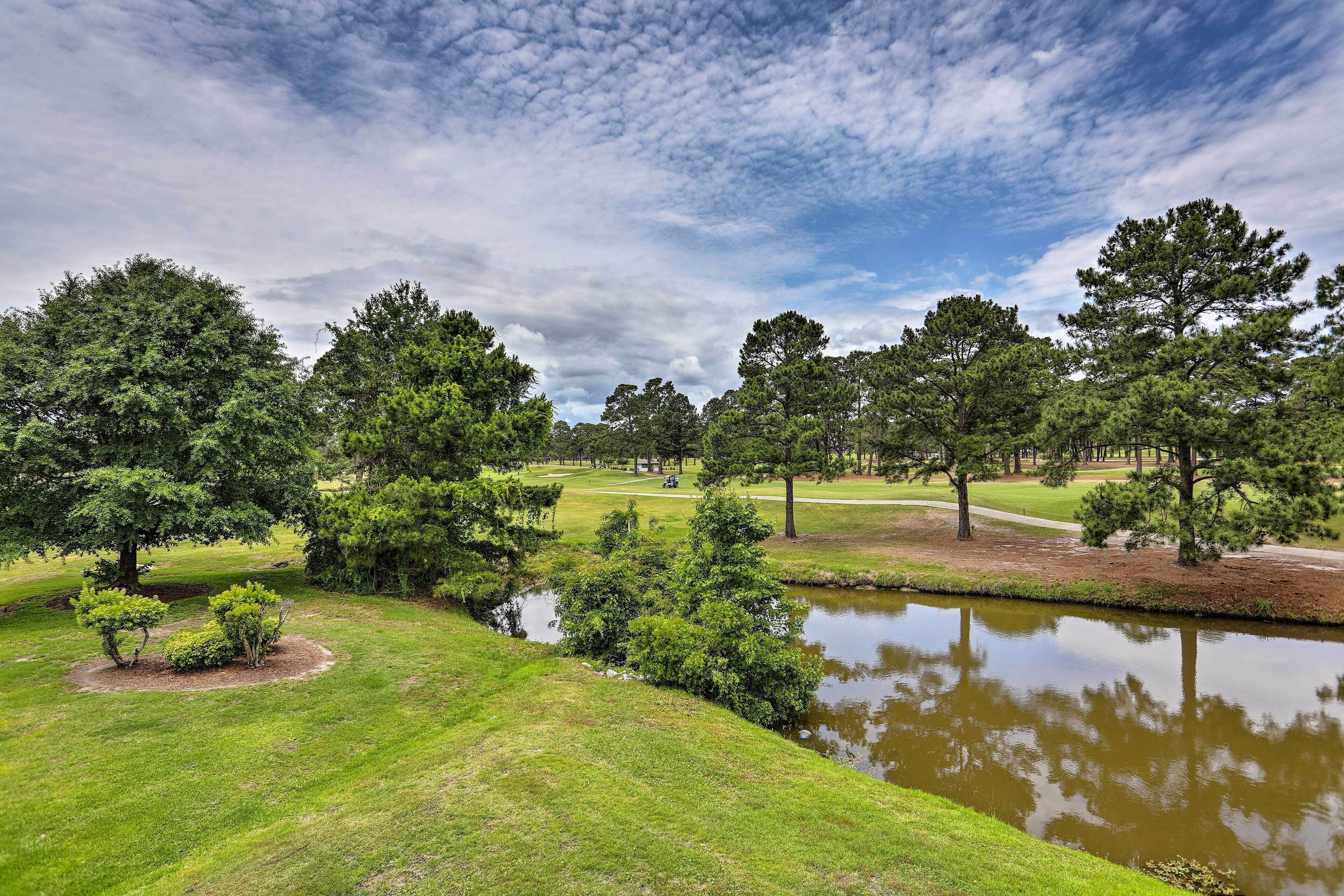A golf course with a pond, surrounded by trees and grassy areas.