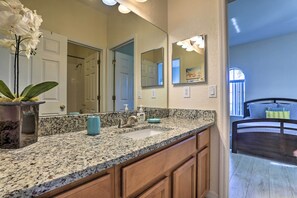 Une salle de bain avec un comptoir en granit, un lavabo, un miroir et une orchidée en pot.
