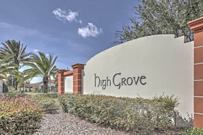 A curved wall with "High Grove" written on it, surrounded by greenery and palm trees.