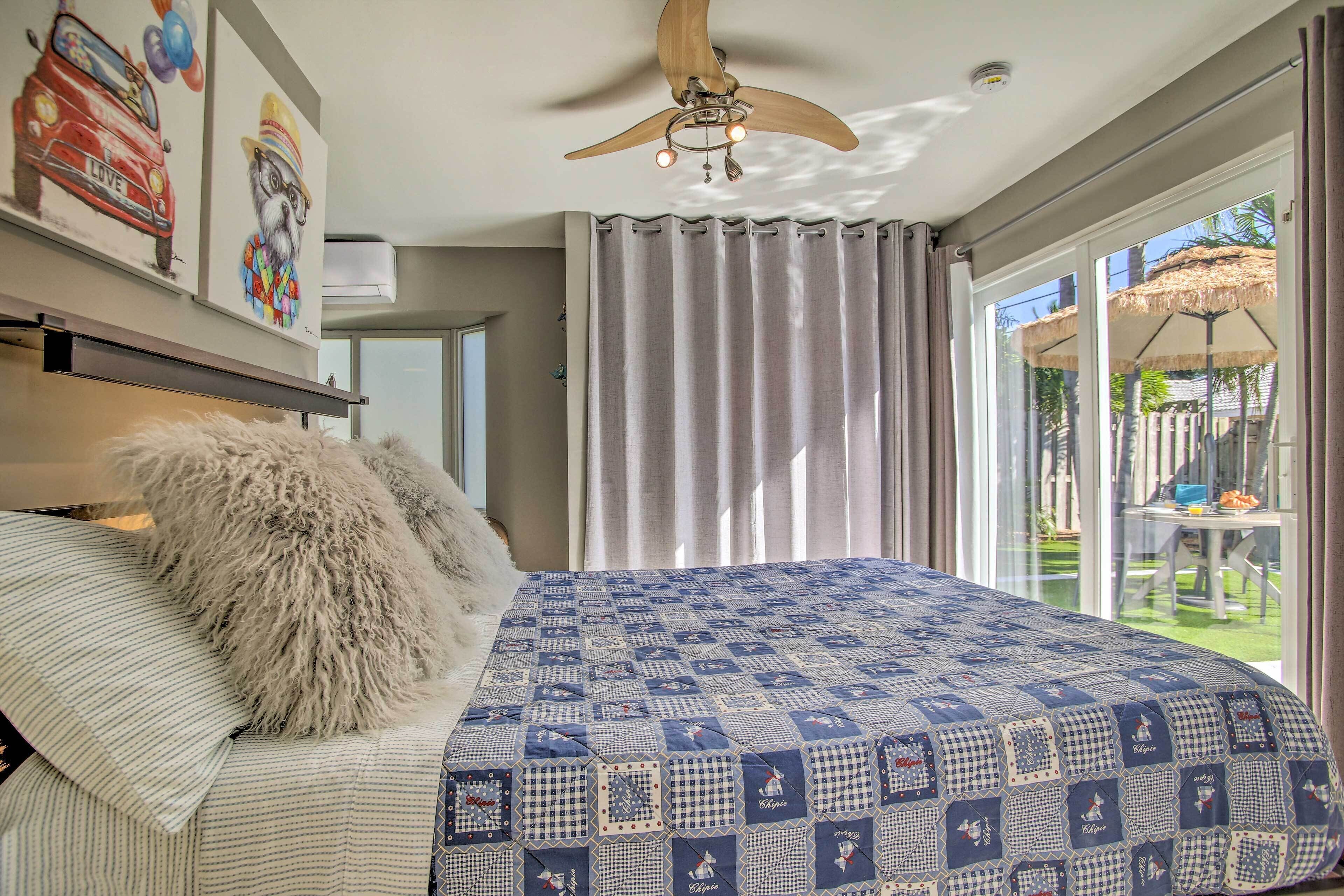 A bedroom with a large bed, a ceiling fan, and a view of the outdoors through a sliding glass door.
