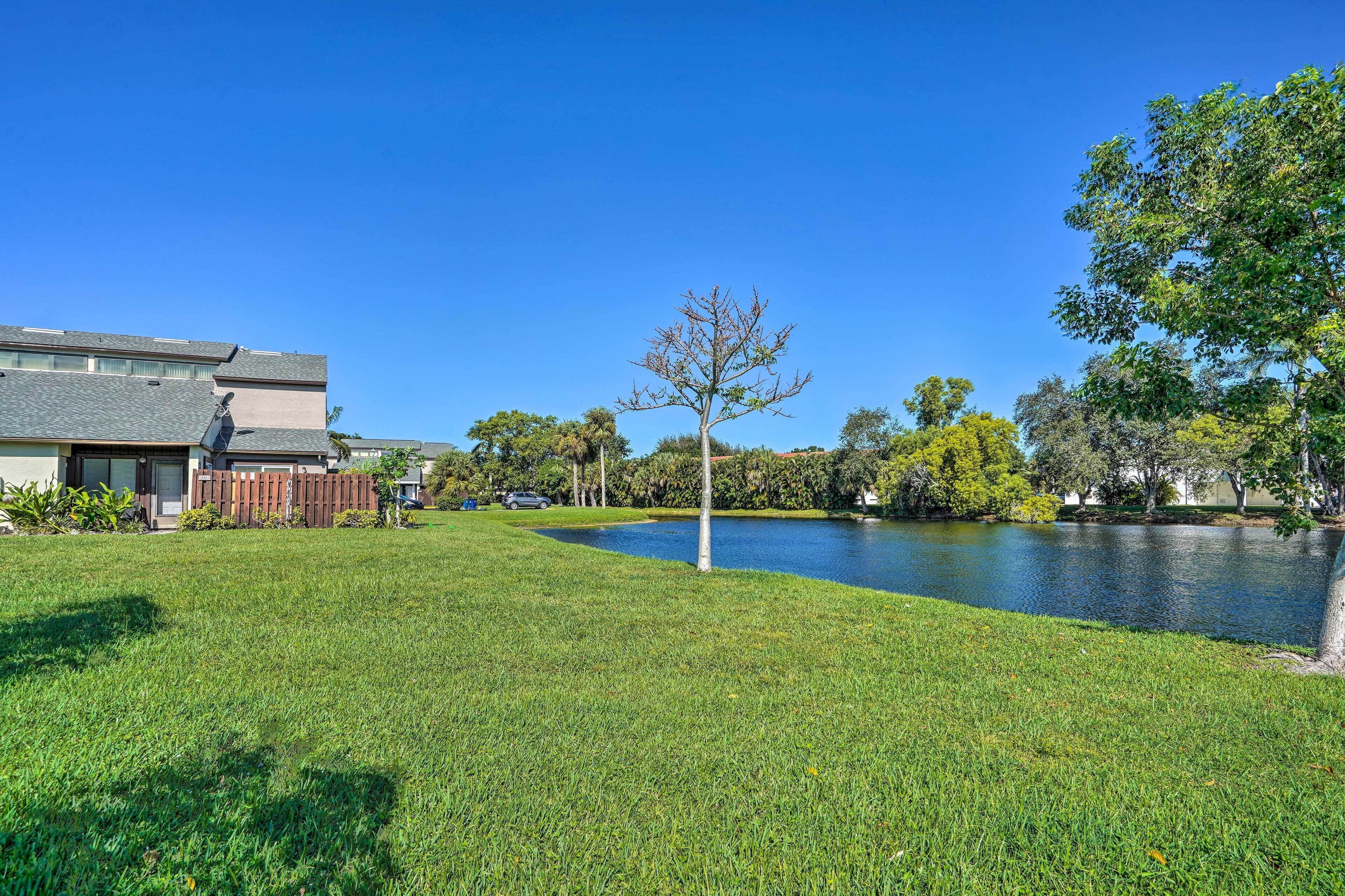 A grassy area with a pond, trees, and a building with a sloped roof.