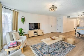A modern living room with a sofa, coffee table, and TV stand. There is a dining area with a table and chairs.