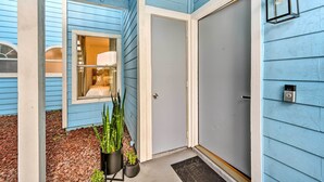 Ein blaues Haus mit geschlossener Tür, einem Fenster mit Lampe im Inneren und einem Blumentopf vor der Fassade.