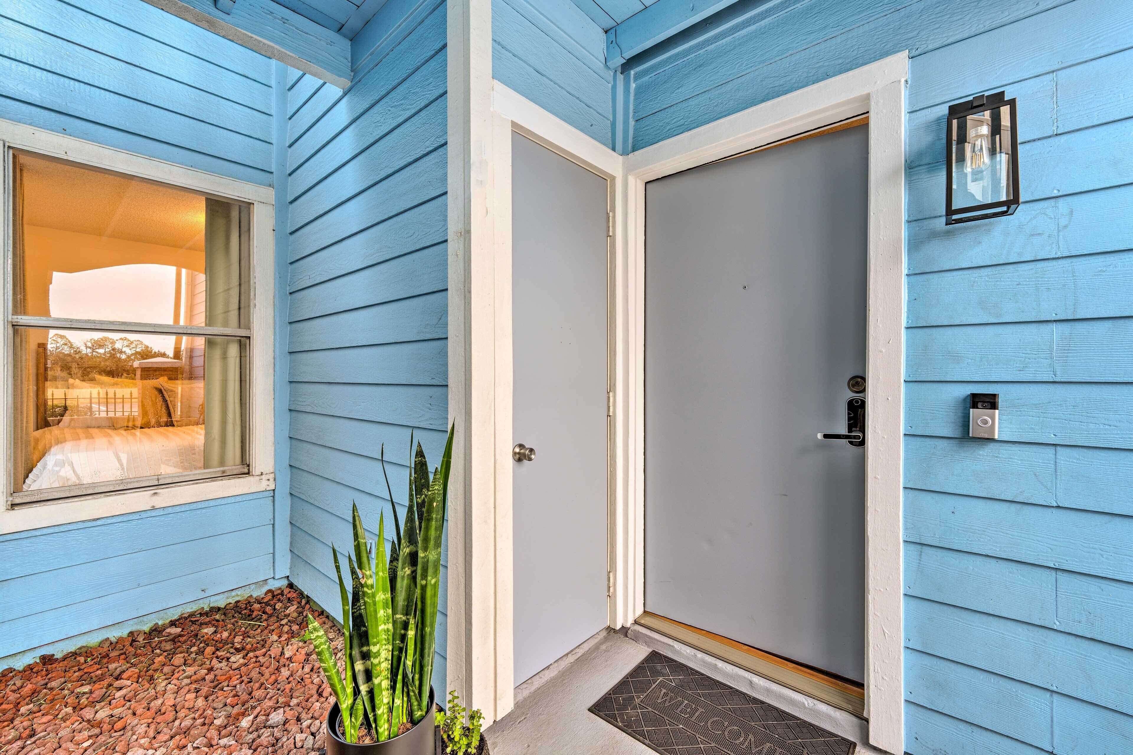 Uma casa azul com porta branca, uma janela, um tapete de boas-vindas e um vaso com planta.
