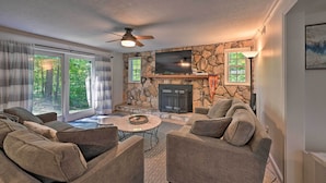 A living room with a stone fireplace, a flat-screen TV, and a ceiling fan. - Chic House w/ Private Dock on Lake Hartwell! (Townville)