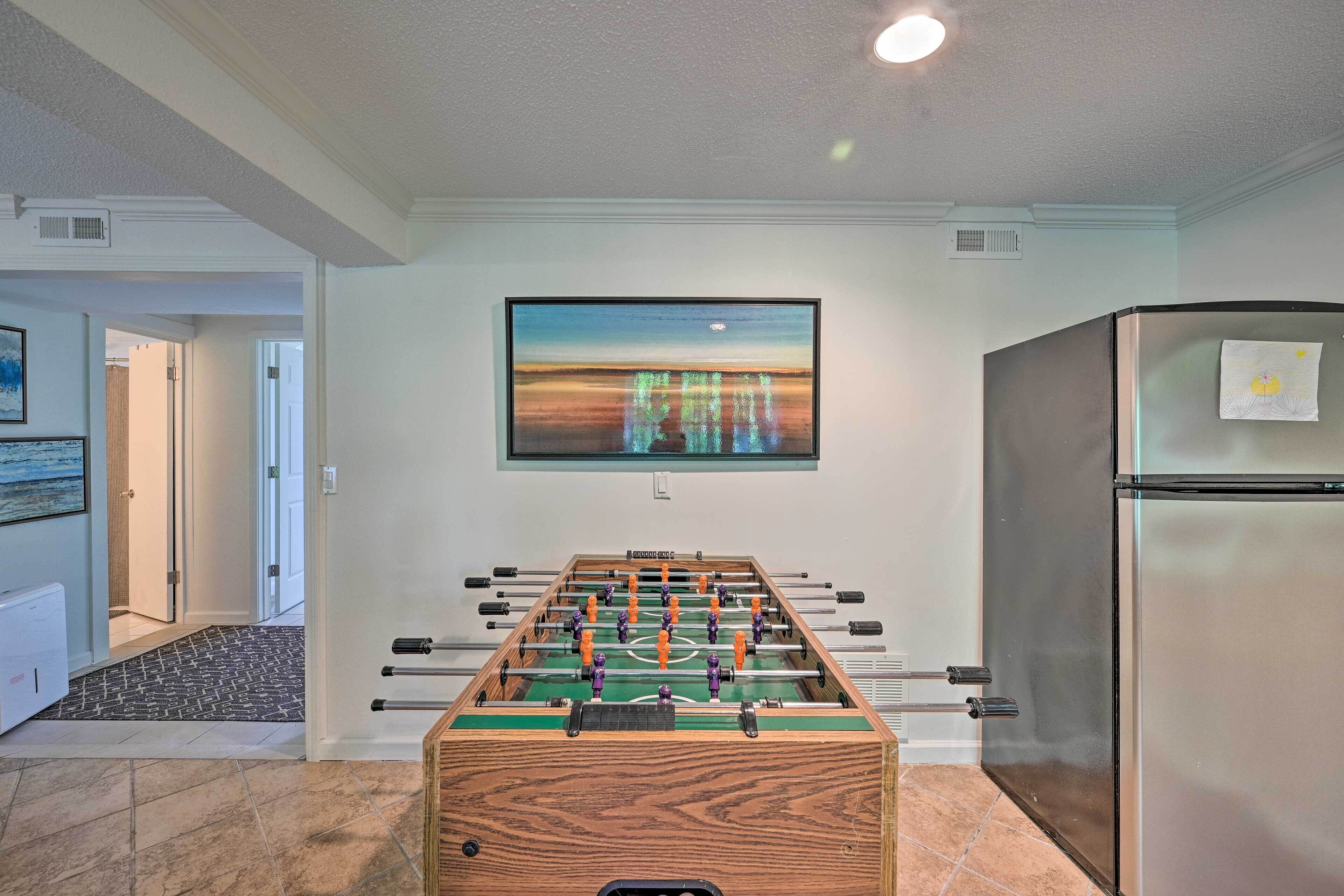 A room with a foosball table, a refrigerator, and a painting on the wall.