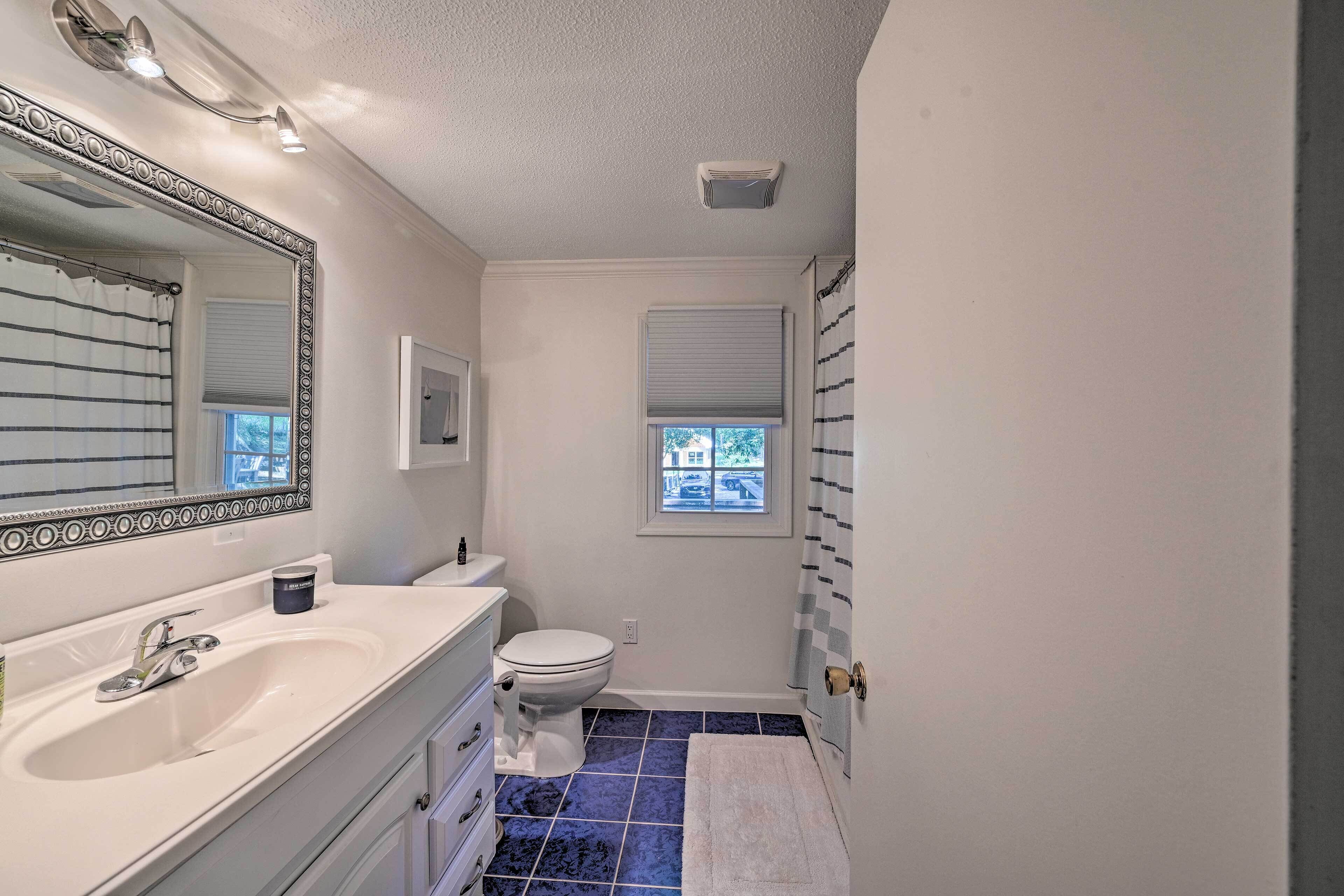 A bathroom with a white sink, a toilet, a large mirror, and a window with blinds.