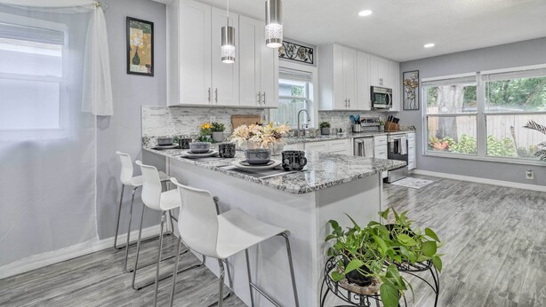Una cocina moderna con armarios blancos, encimera de granito e isla central con taburetes de bar.