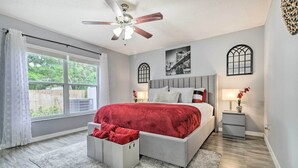 Un dormitorio con cama, ventilador de techo, ventana y mesita de noche.