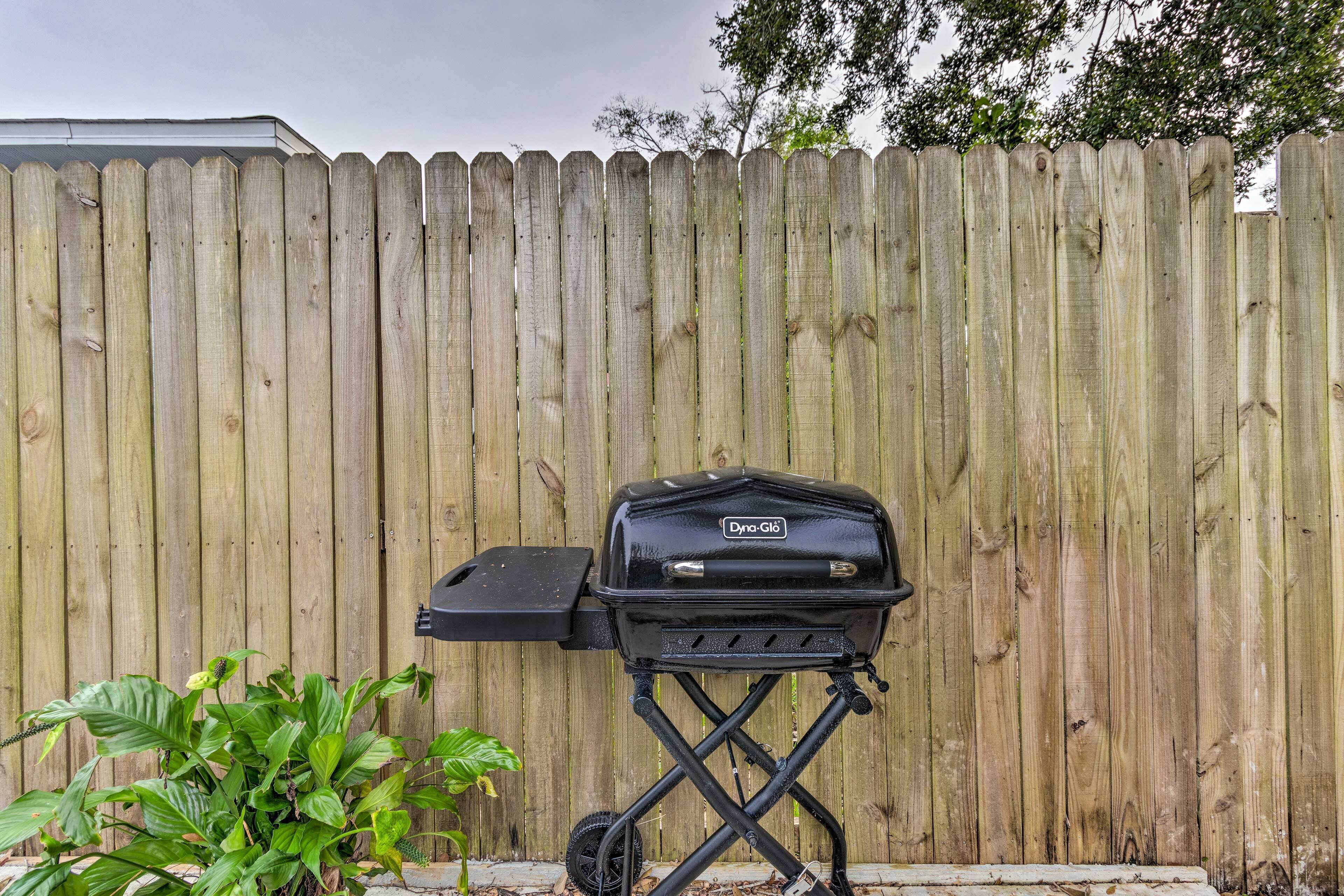 A portable grill with wheels against a wooden fence.