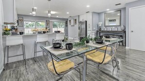 Una cocina moderna con una isla central, taburetes de bar y una mesa de comedor con cubierta de vidrio.