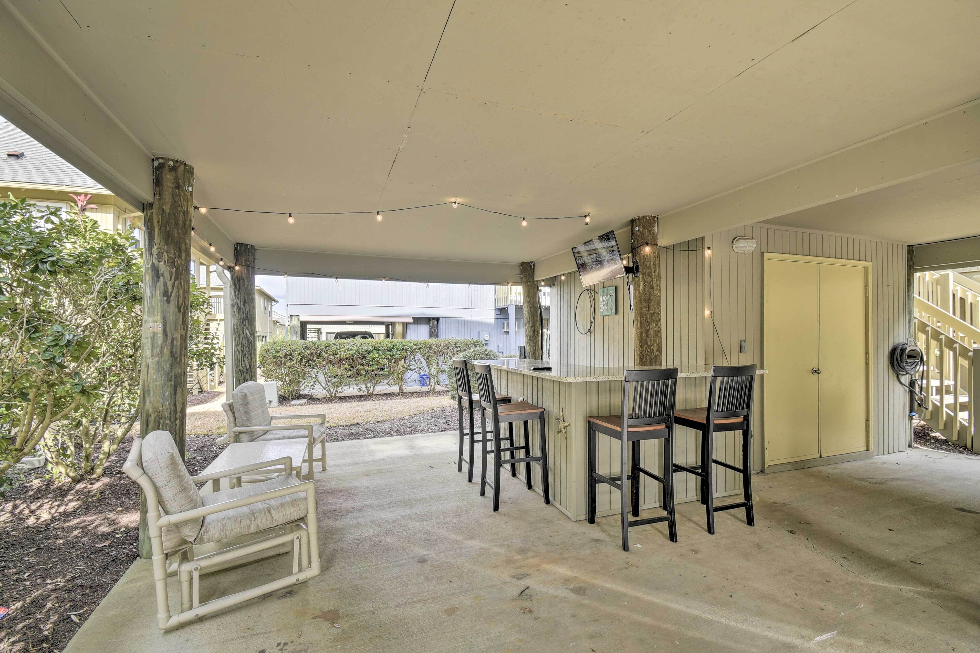 A covered outdoor seating area with a bar, chairs, and a concrete floor.
