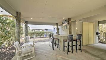 A covered outdoor seating area with a bar, chairs, and a concrete floor.