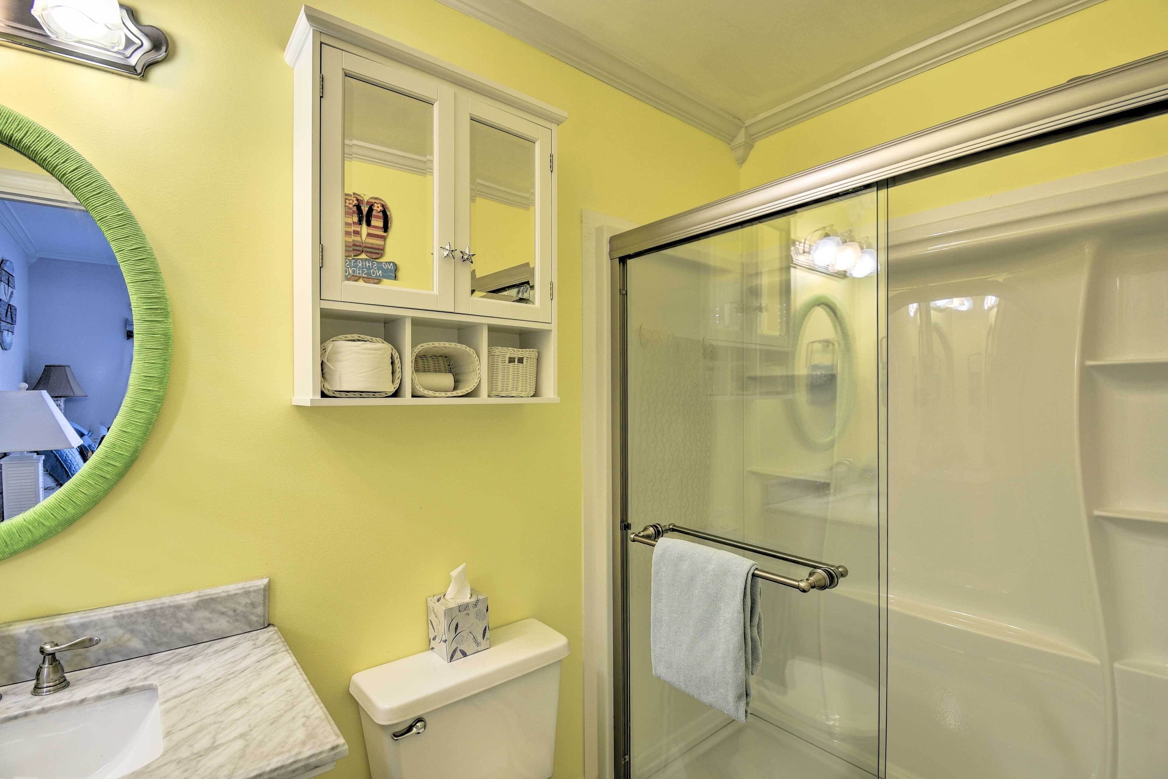 Une salle de bain avec une douche à parois de verre, des toilettes blanches, un lavabo en marbre et un miroir avec un cadre vert.