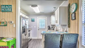 Een keuken met een houten wand, een klok en een bord met daarop 'BEACH HOUSE'.