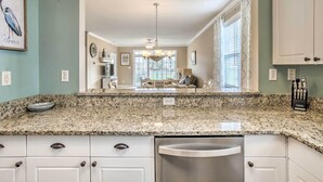 A kitchen with granite countertops, white cabinets, and a stainless steel dishwasher. - Pool, Beach & Golf: Barefoot Resort Condo! (North Myrtle Beach)