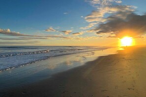 Uma praia com um pôr do sol, ondas e pegadas.