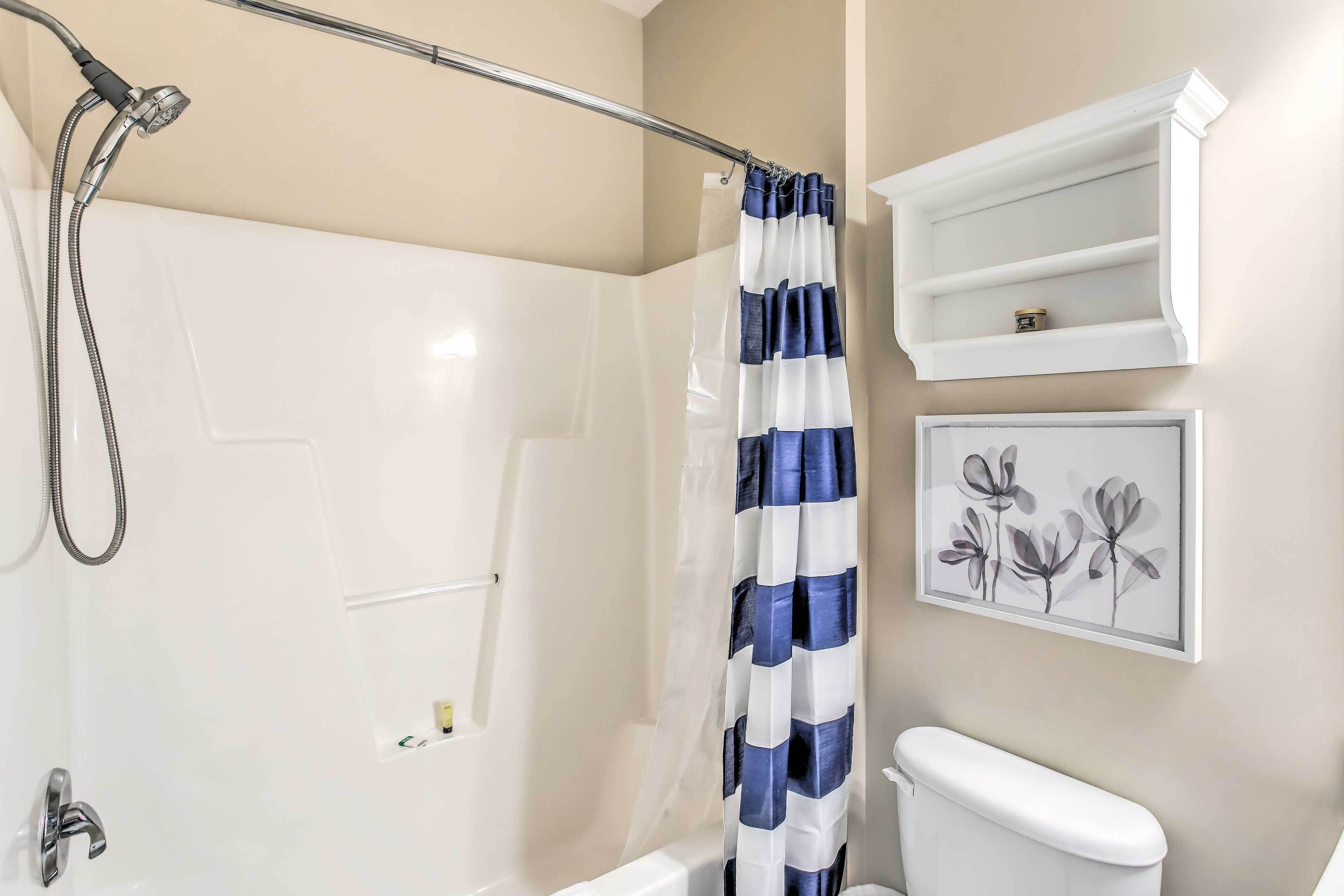 A bathroom with a shower, toilet, and a shelf with a framed picture.