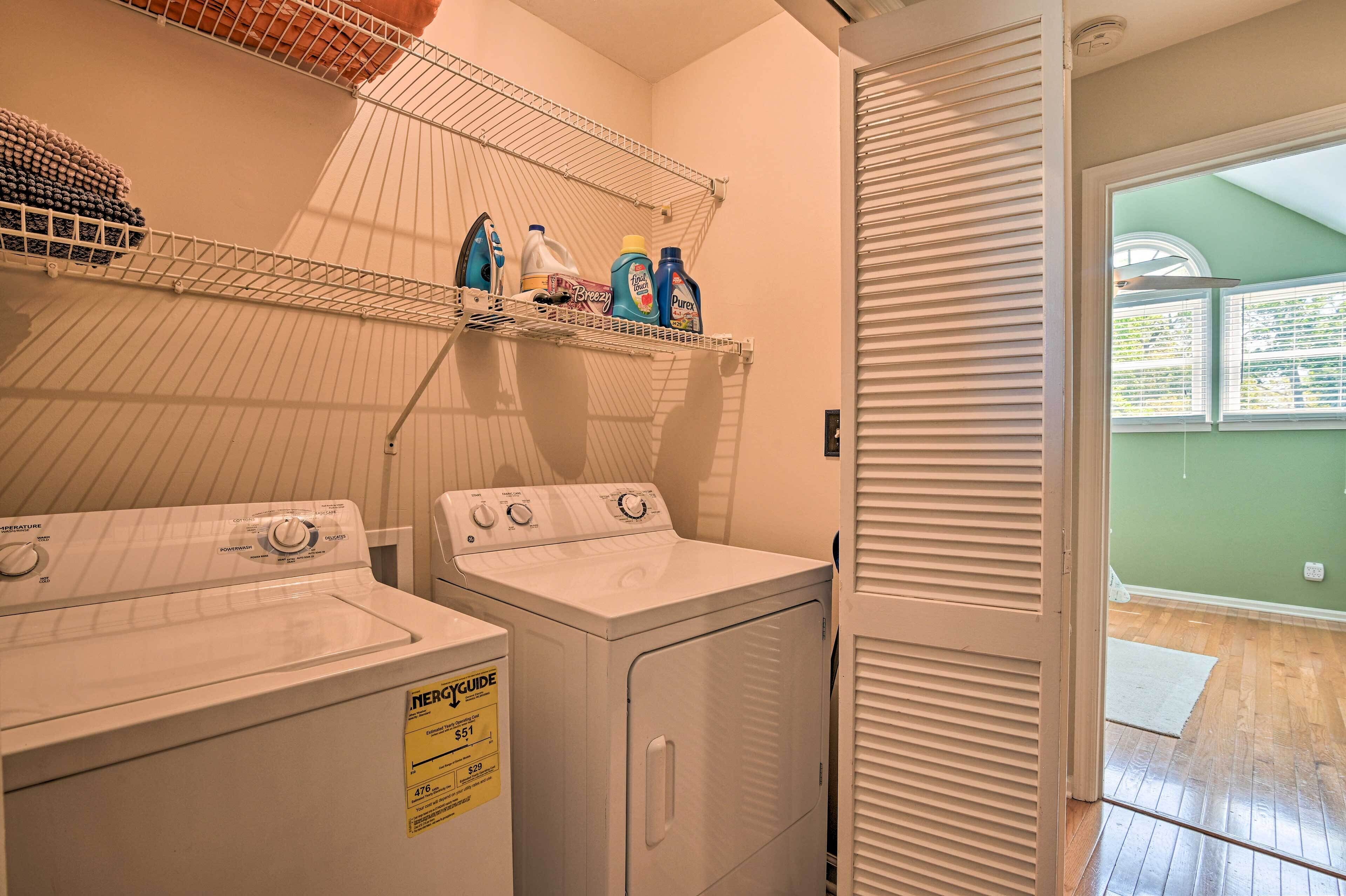 Un área de lavandería con dos lavadoras, un tendedero con botellas de detergente y una puerta que da a una habitación con vistas.