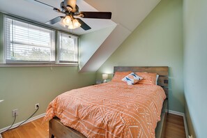 A bedroom with a sloped ceiling, a bed with an orange patterned bedspread, a ceiling fan, and a window with blinds. - Coastal Vacation Rental - 2 Mi to Huntington Beach (Murrells Inlet)