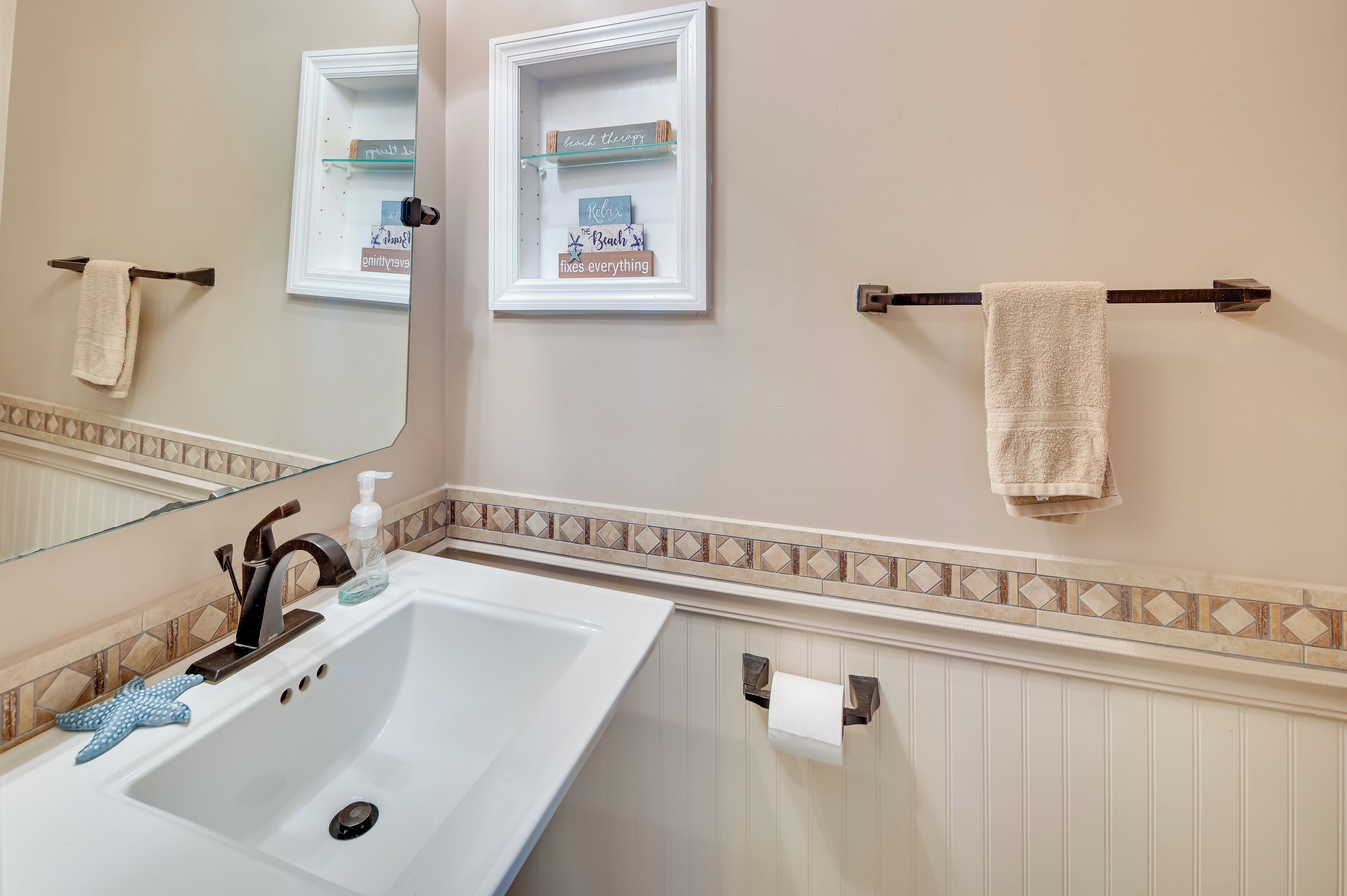 A bathroom with a white sink, a mirror, a towel rack, and a glass shelf with decorative items.