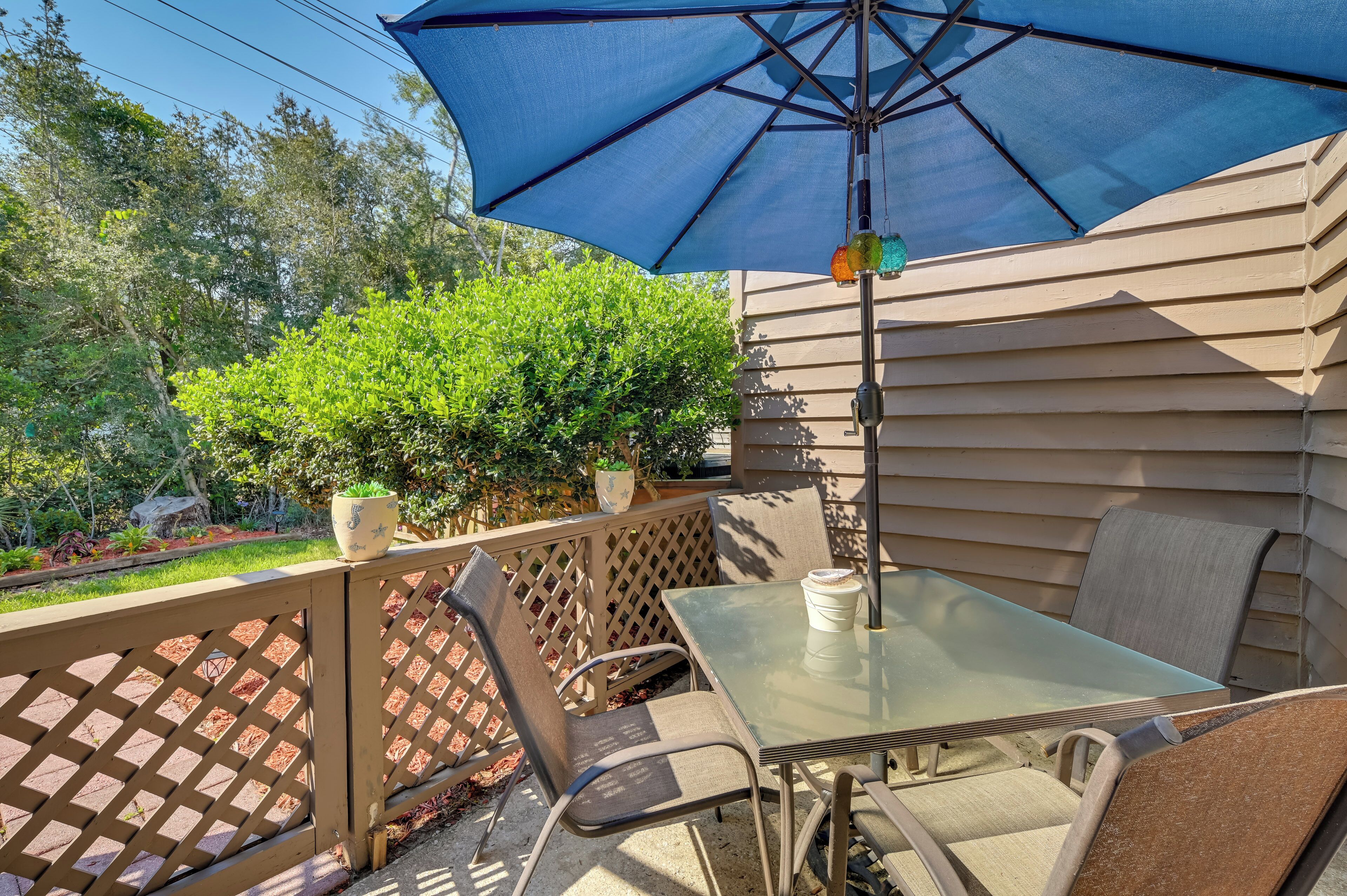Un patio con una mesa y sillas de vidrio, una sombrilla azul y una valla de madera.