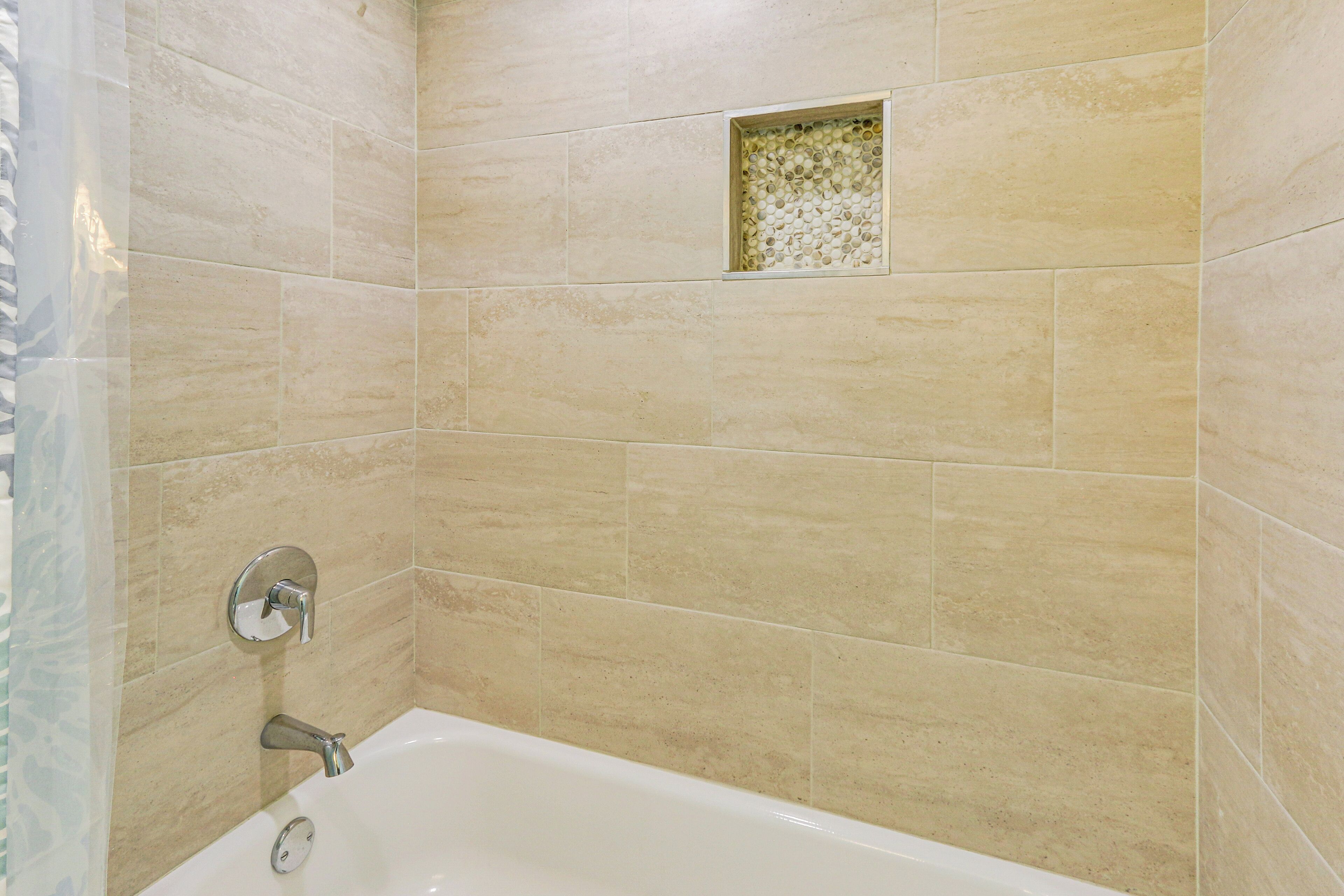 Un baño con azulejos color beige, una bañera y un pequeño azulejo decorativo en la pared.