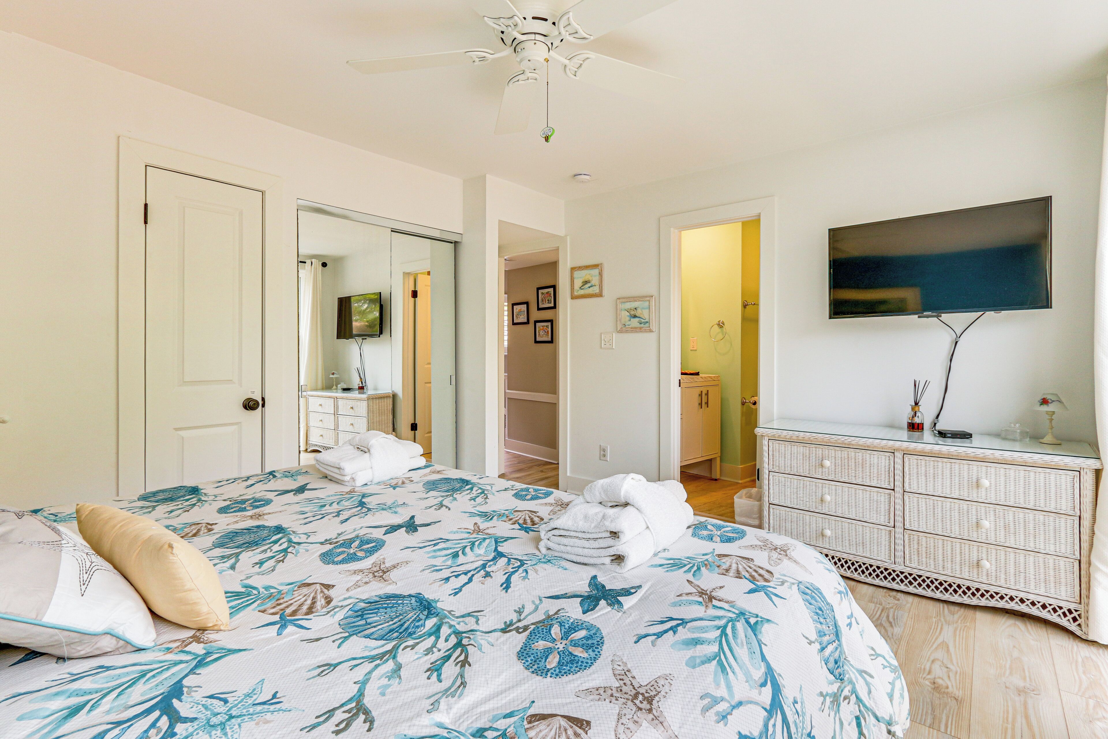 A bedroom with a bed, a dresser, a television, and a ceiling fan.