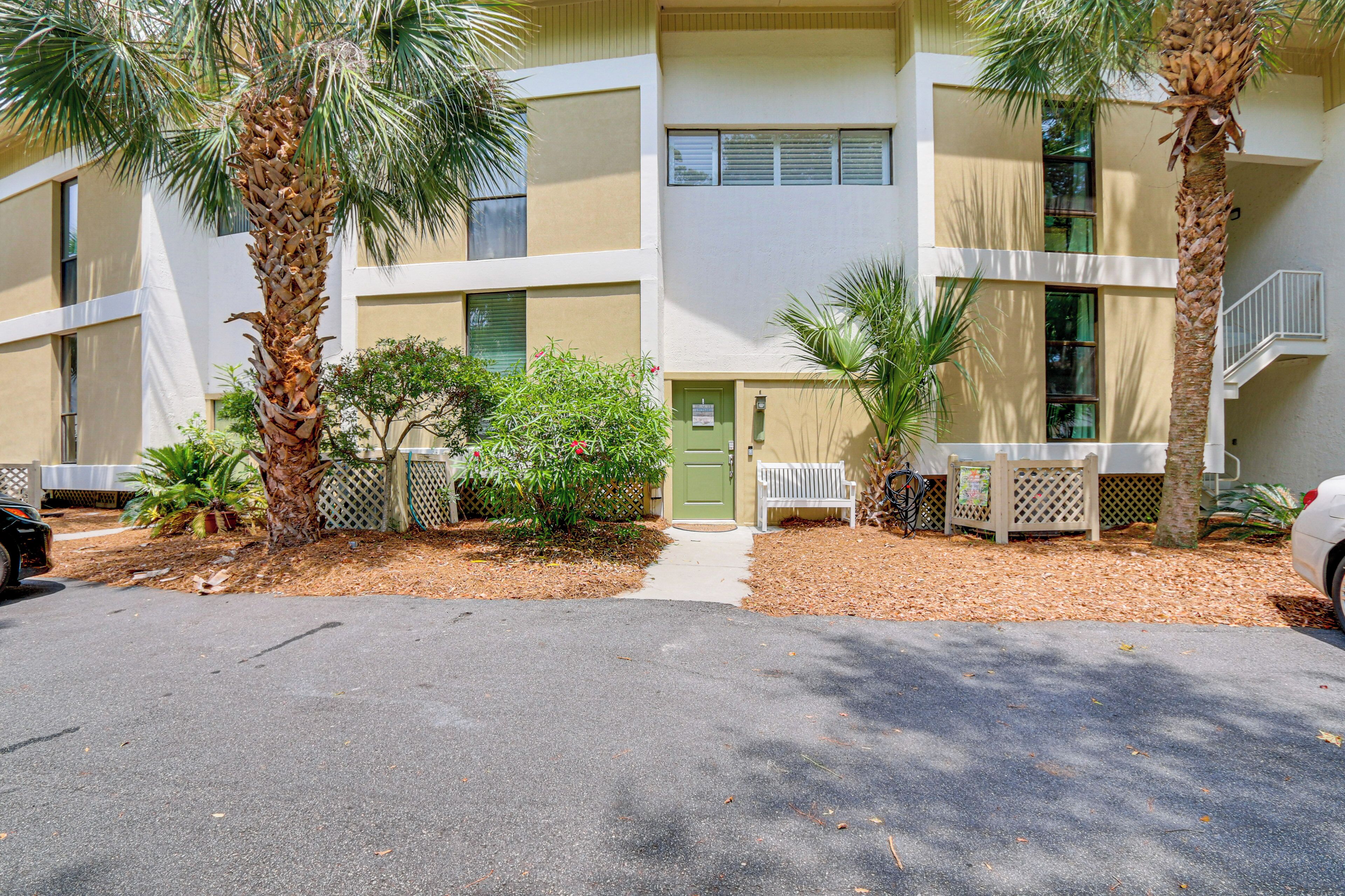 A multi-story building with a flat roof, a green door, and a small front yard with palm trees and shrubs.
