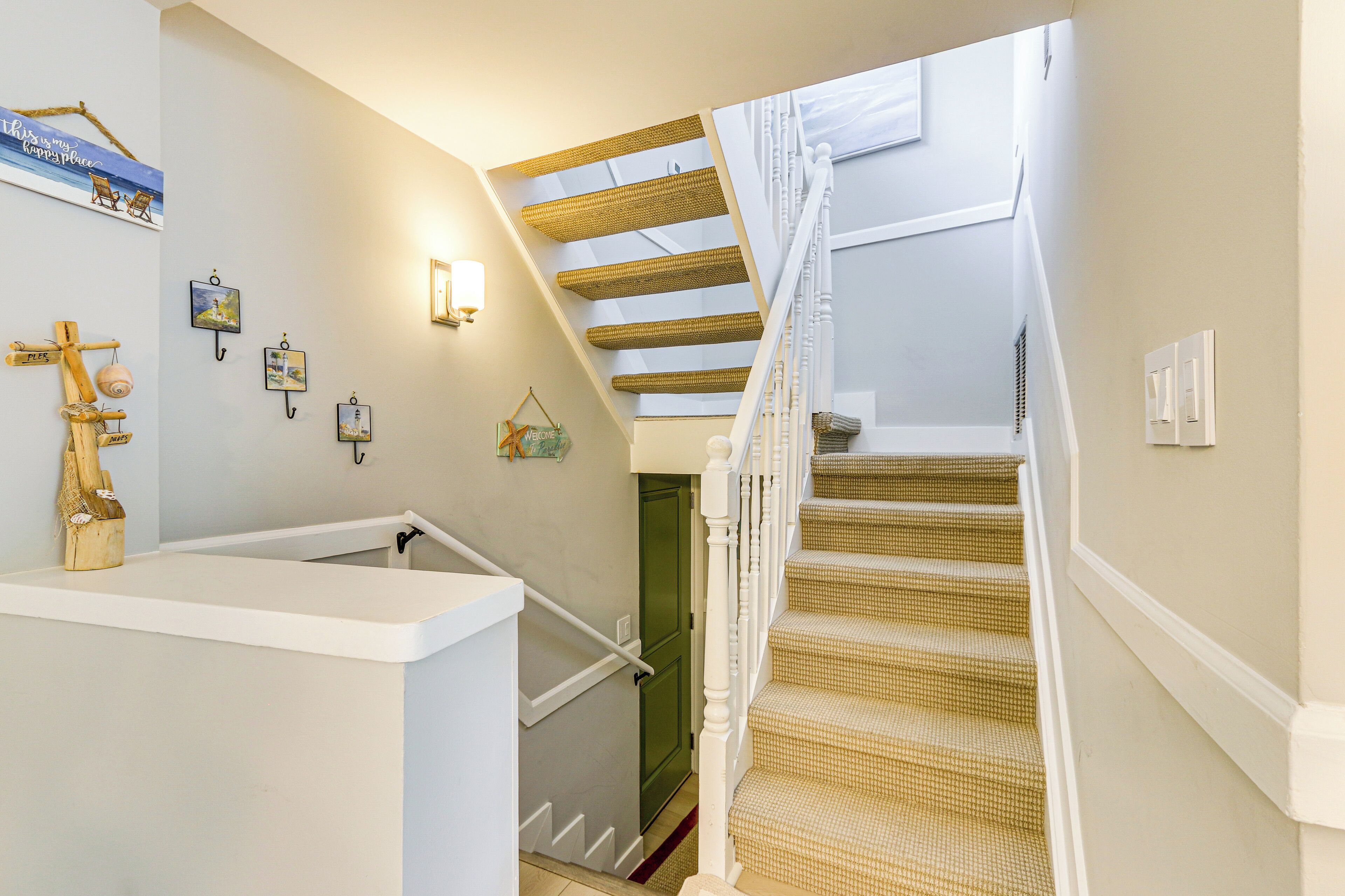 A staircase with a woven handrail and a white wall with a picture frame and a light fixture.
