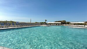 A clear blue pool with lounge chairs and umbrellas, surrounded by a fence and palm trees. - Pool, Spa & Dining: Beach Condo in Hilton Head! (Hilton Head Island)