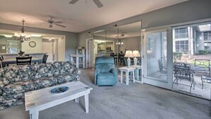 A living room with a sofa, armchair, coffee table, and a dining area with a table and chairs. There is a large mirror reflecting the room and a ceiling fan. - 4 Mi to Ocean: Golf Resort Condo in N Myrtle Beach (North Myrtle Beach)