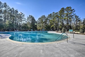 A swimming pool with a curved edge, surrounded by trees and lounge chairs. - 4 Mi to Ocean: Golf Resort Condo in N Myrtle Beach (North Myrtle Beach)