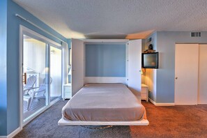 A bedroom with a bed, a sliding glass door leading to a balcony, a television, and a nightstand. - Cozy Destin Studio w/ Shared Pools + Beach Access! (Destin)