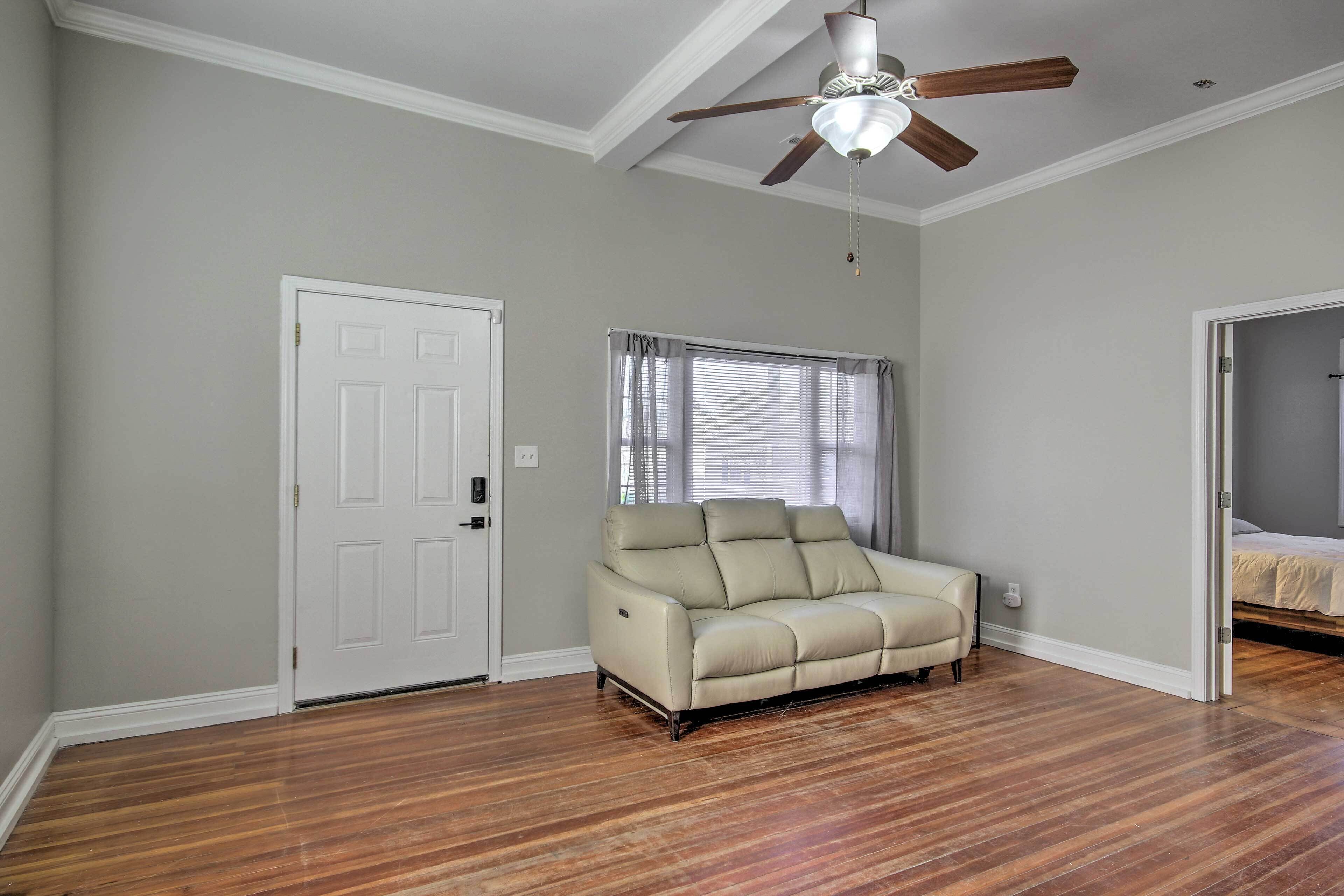 A room with a beige sofa, wooden flooring, a ceiling fan, and a door.