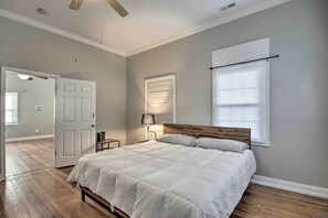 A bedroom with a large bed, a wooden headboard, a nightstand, a lamp, and a window with blinds.