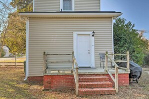 A two-story house with a front porch, a white door, and a small outdoor seating area.