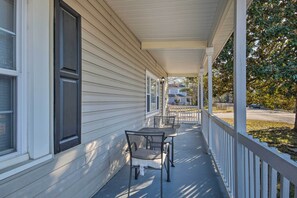 A covered porch with a table and chairs, a white railing, and a view of the street.