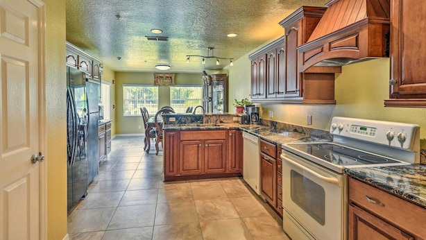 A kitchen with wooden cabinets, a granite countertop, a stainless steel refrigerator, and a built-in oven. - Cozy Coastal Retreat w/ Grill < 5 Mi to Beach (Port Orange)