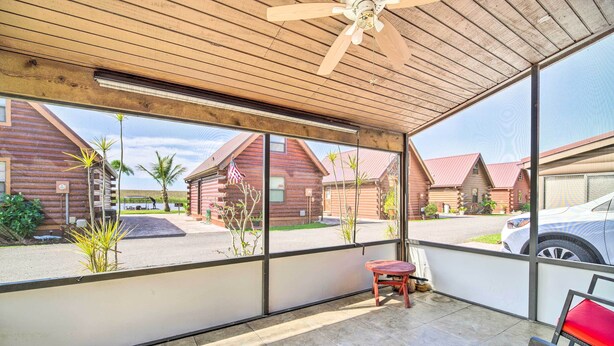 A covered patio with a ceiling fan, large windows, and a view of log cabins. - Okeechobee Cabin in Waterfront Community w/ Dock! (Okeechobee)