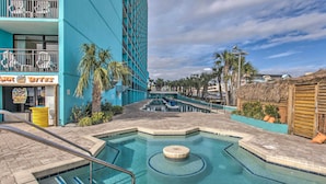 Zona de piscina con un edificio azul, palmeras y un letrero que dice 'Shark Bites'.
