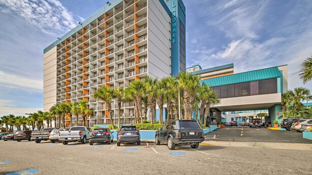 Un hotel de varios pisos con un llamativo letrero 'LANDMARK', un estacionamiento con varios vehículos y palmeras en primer plano.