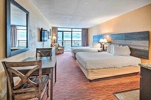 A hotel room with two beds, a desk, and a chair. There is a TV mounted on the wall, and the room has a large window with curtains. - Cozy Studio Condo w/ Resort Amenities Access! (Myrtle Beach)