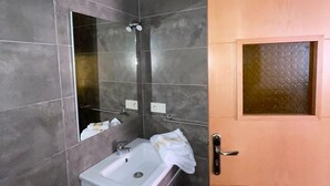 Ein Badezimmer mit dunklen Fliesen, einem weißen Waschbecken, einem Spiegel und einer Holztür.